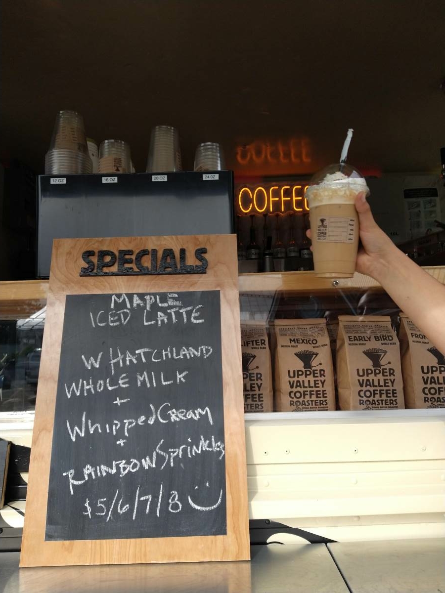 iced latte held up in front of the Specials menu board
