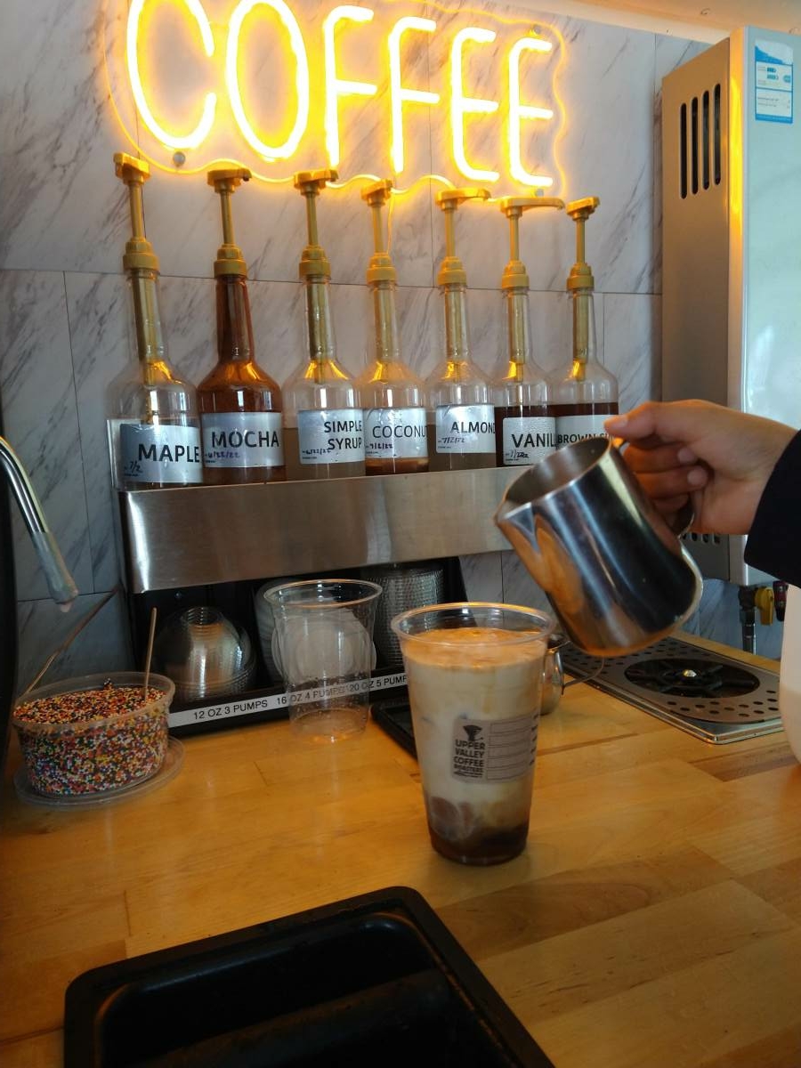 Milk pour into iced coffee in front of the syrup station.